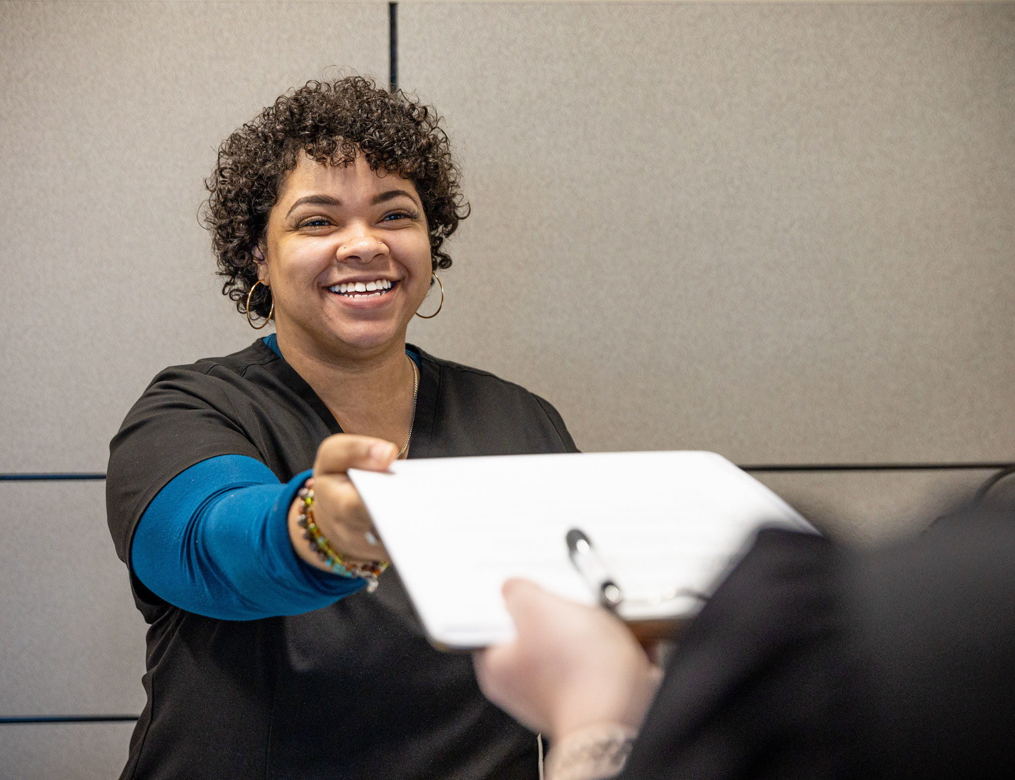 A smiling receptionist hands a patient a clipboard to prepare for sports physicals in Fergus Falls