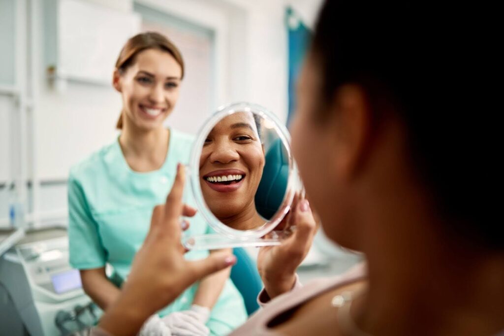 A doctor smiles while a patient admires her skin in a handheld mirror after receiving an anti-aging treatment in Fargo